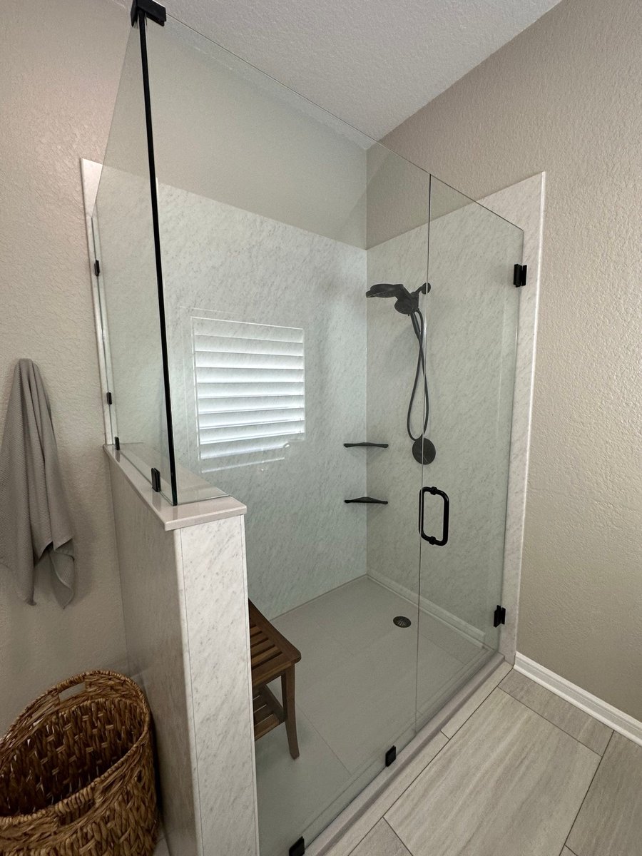 Marble walk-in shower with frameless glass, black fixtures, and teak bench