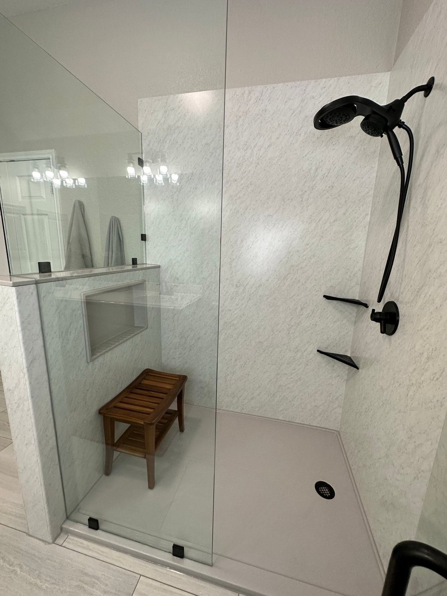 Marble shower with black hardware, corner shelves, and teak bench inside glass
