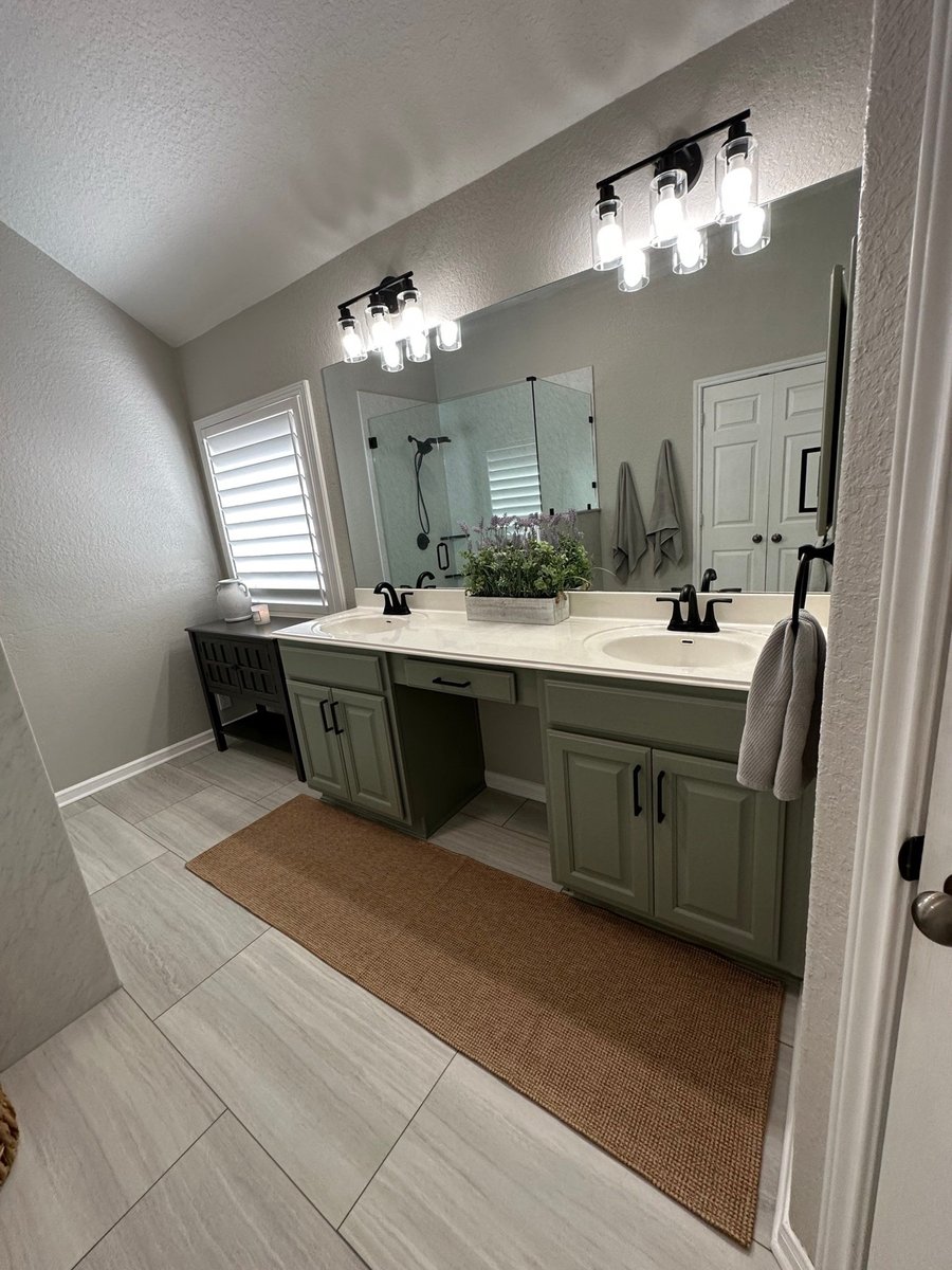 Double vanity with green cabinets, white counter, and black-framed mirror