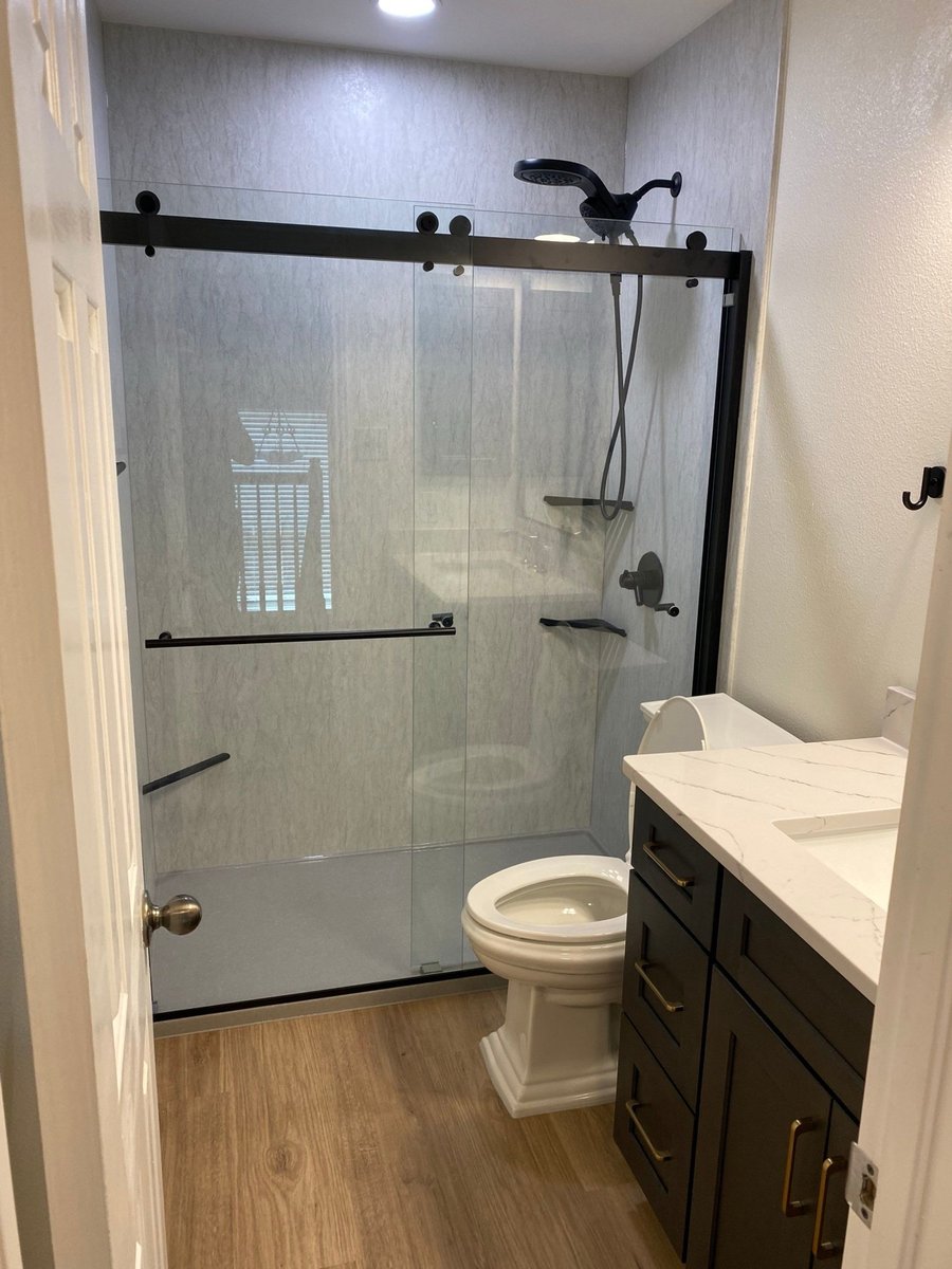 Walk-in shower with sliding glass door, matte black fixtures, and gray stone wall panels
