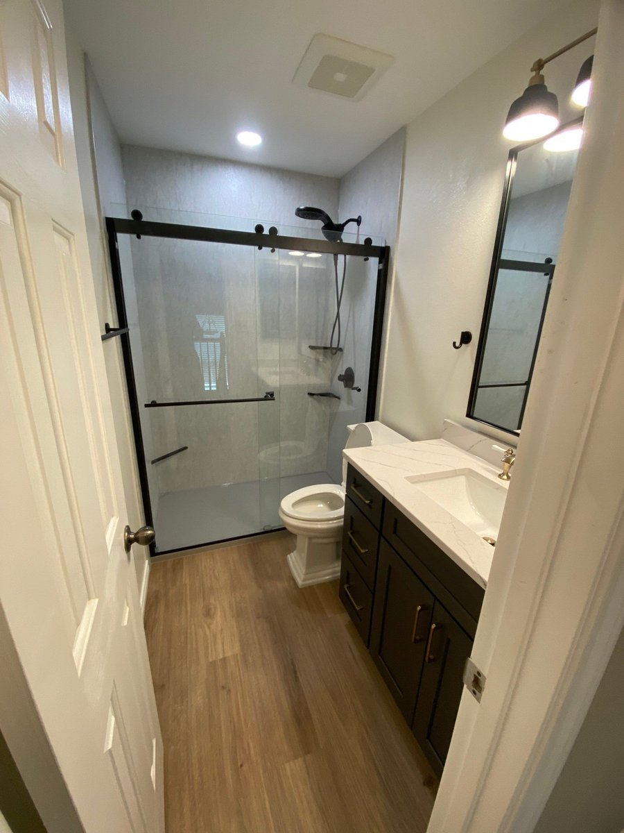 Remodeled bathroom with glass shower, dark vanity, white quartz counter, and wood-look flooring