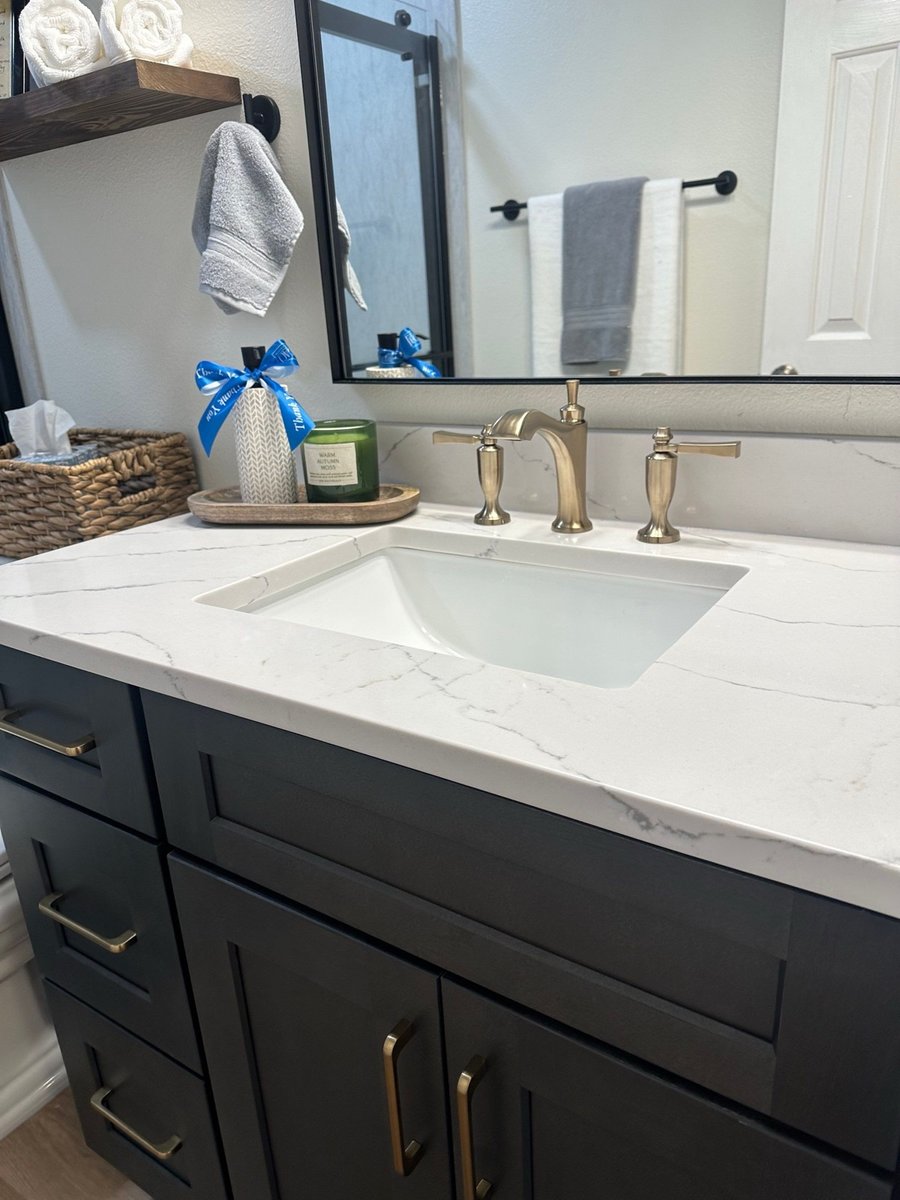 Close-up of white quartz vanity with undermount sink and brushed gold widespread faucet