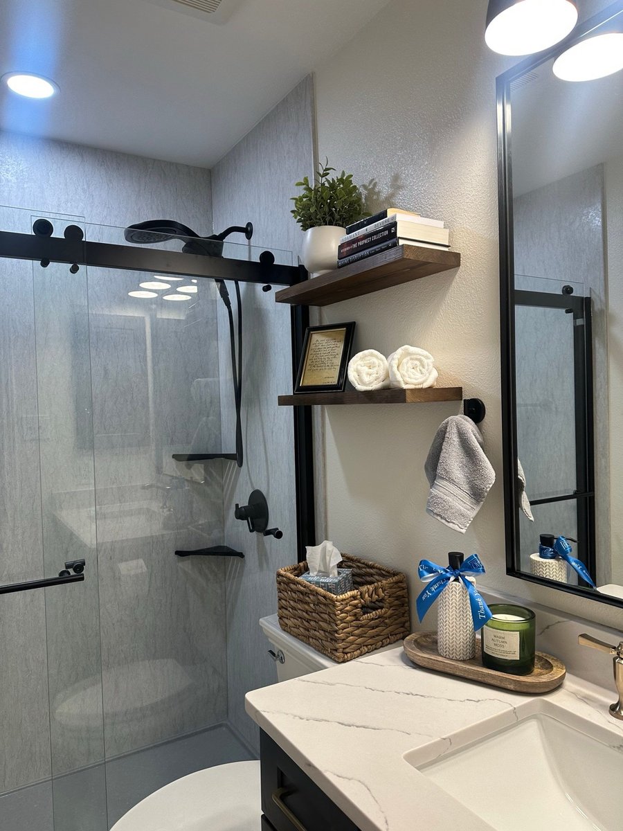 Walk-in shower with black hardware beside floating shelves and decor
