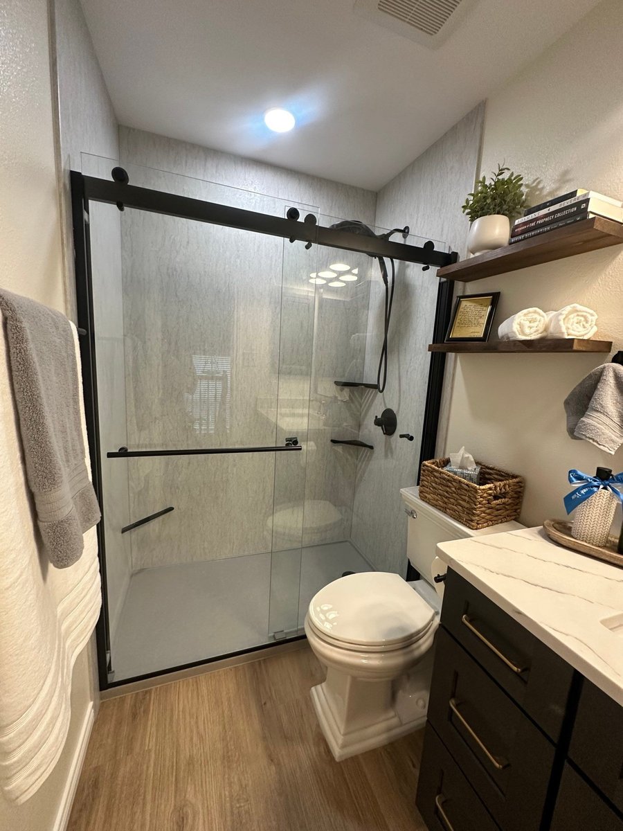 Glass walk-in shower with black trim, toilet, dark vanity, and gray stone walls