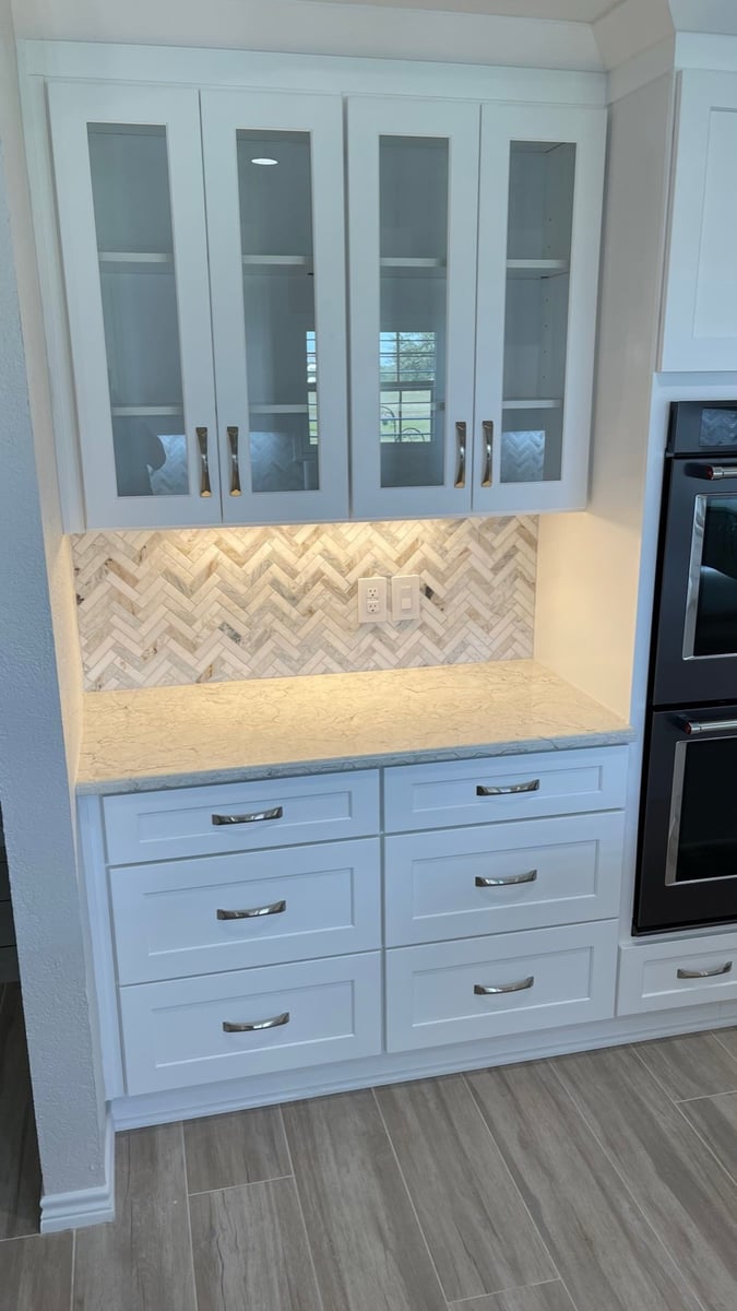 White glass-front display cabinets over a counter with herringbone marble backsplash