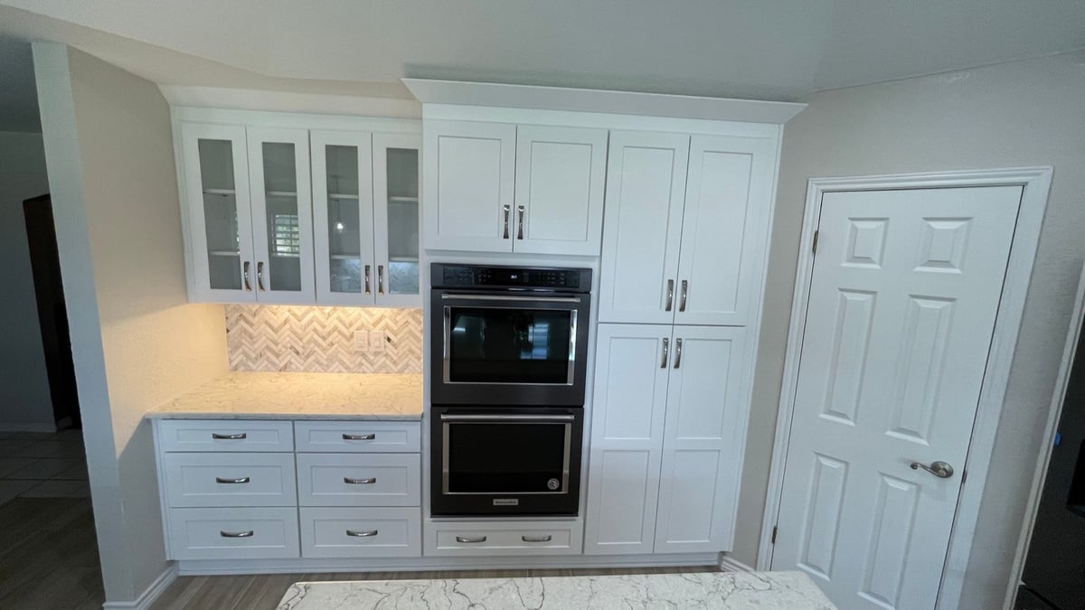 White cabinetry with black double wall ovens flanked by pantry and closet doors
