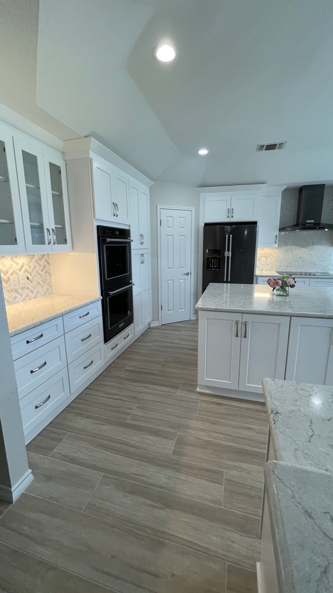 Bright white kitchen with black refrigerator, double ovens and quartz island