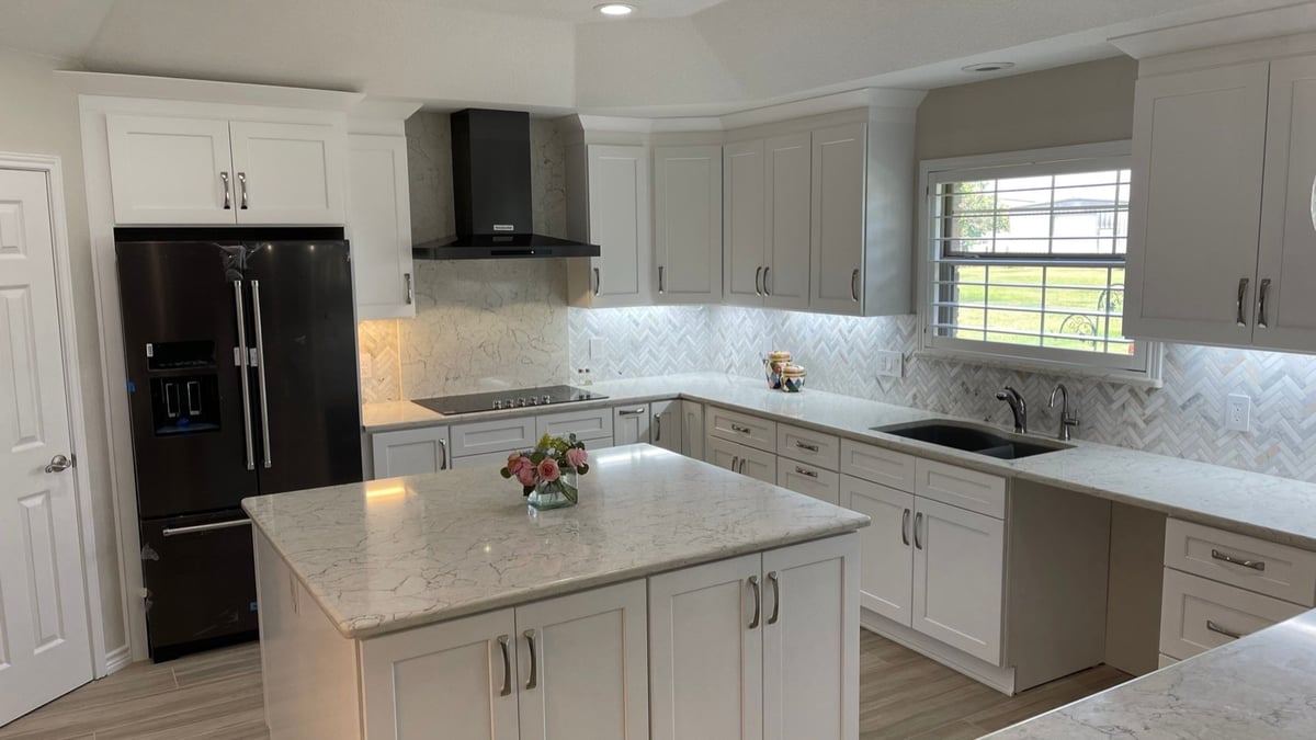 White kitchen with black chimney hood, window over sink and quartz island