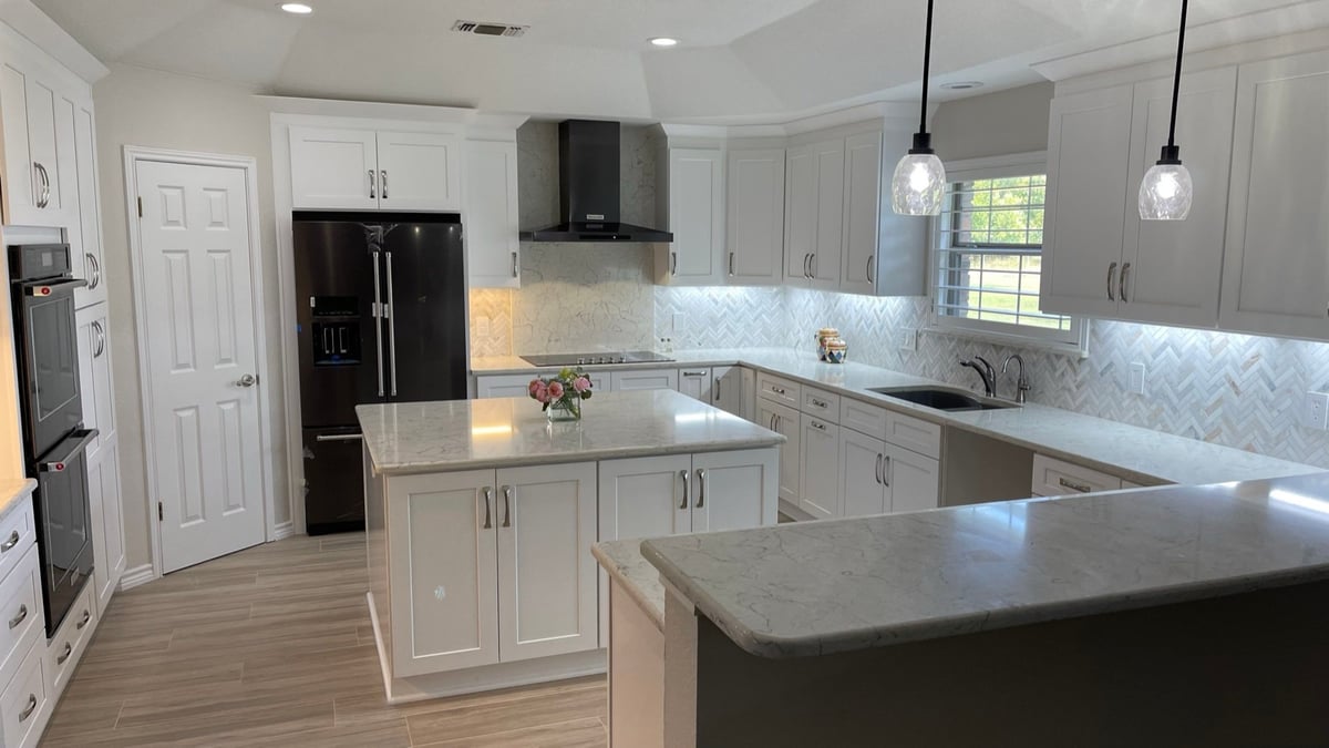 Light gray cabinets with herringbone backsplash and window above the sink