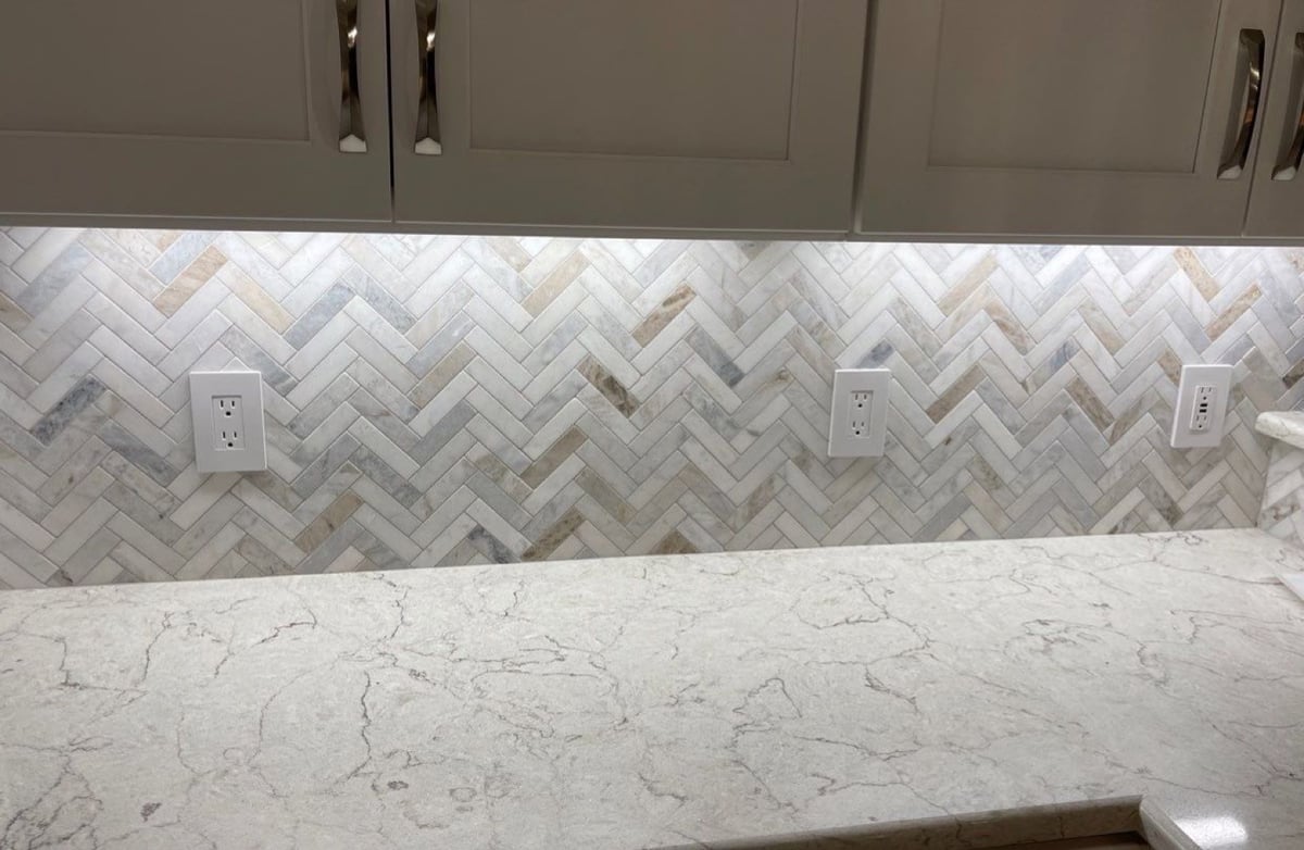 Detail of herringbone marble backsplash above a veined quartz countertop