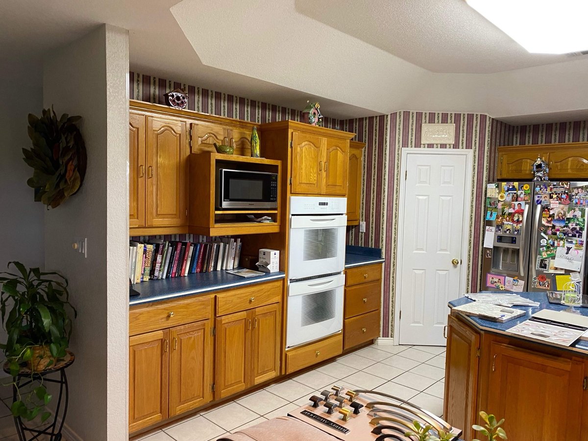 Pre-remodel oak cabinets with white double wall oven and striped wallpaper