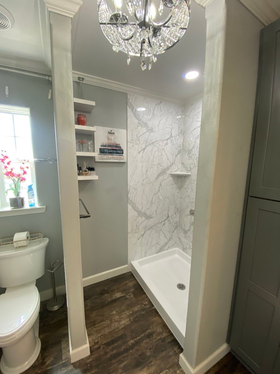 Marble walk-in shower beside built-in shelves, toilet and crystal chandelier
