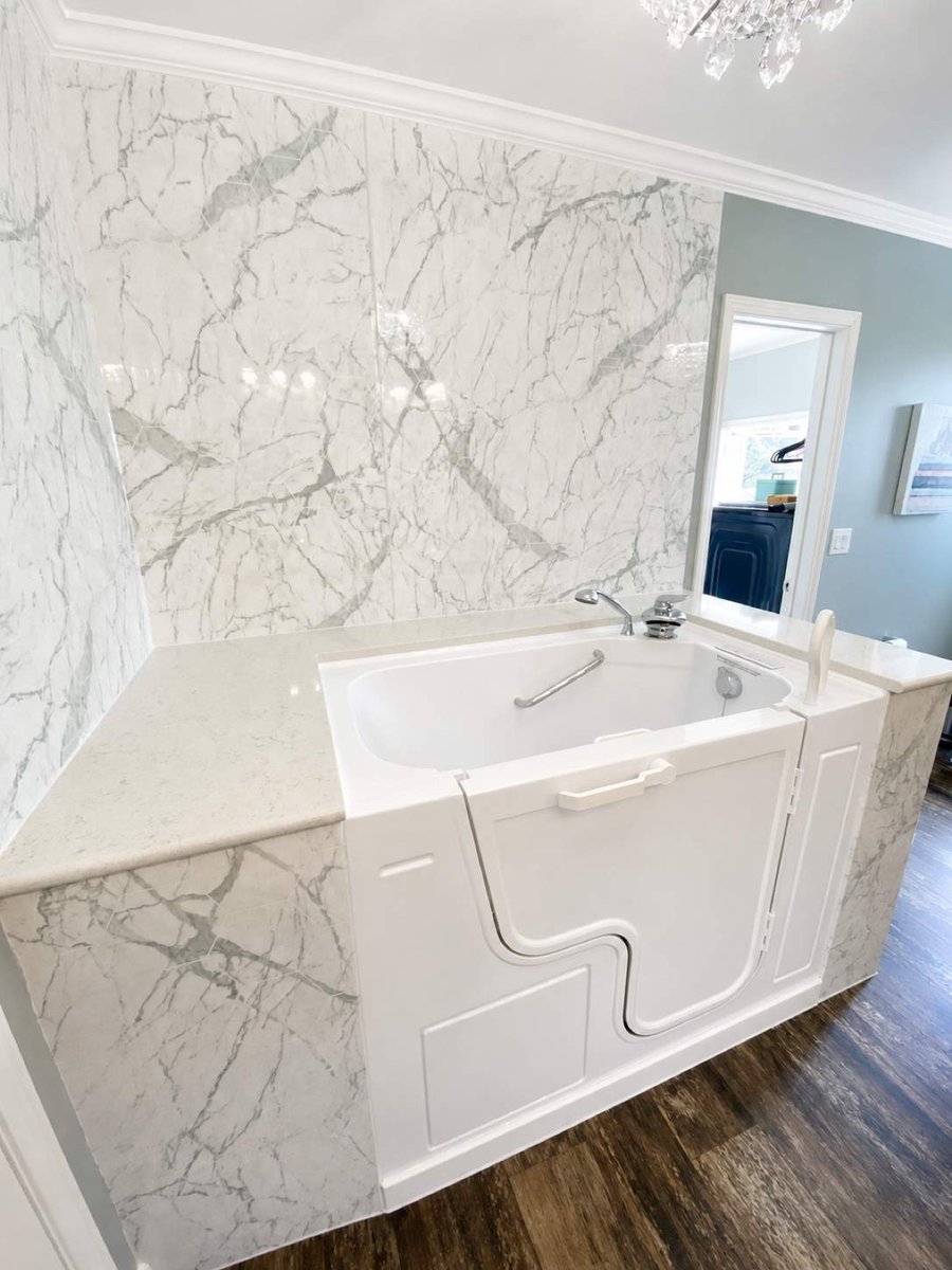 White walk-in soaking tub with side door and marble surround on wood-look floor