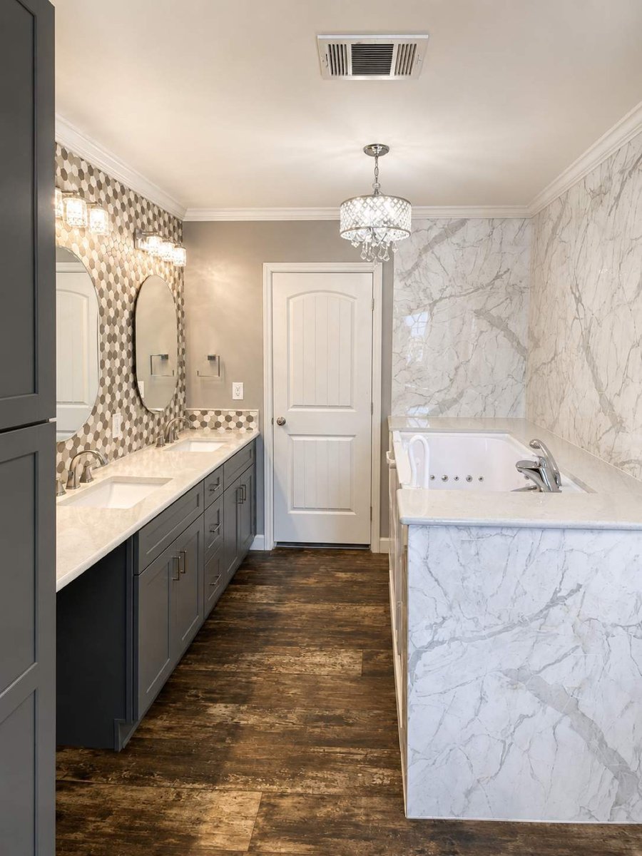 Gray double vanity with oval mirrors, hexagon accent wall and marble walk-in tub