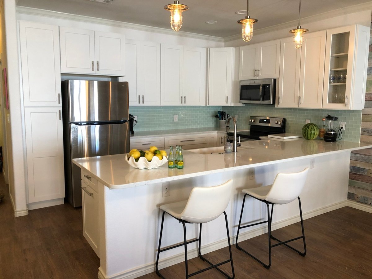 White shaker kitchen with quartz peninsula, glass tile backsplash, and cage pendants