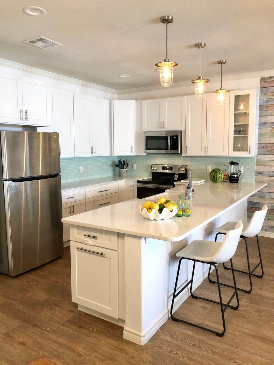 Bright white kitchen with quartz peninsula, barstools, and aqua glass tile backsplash
