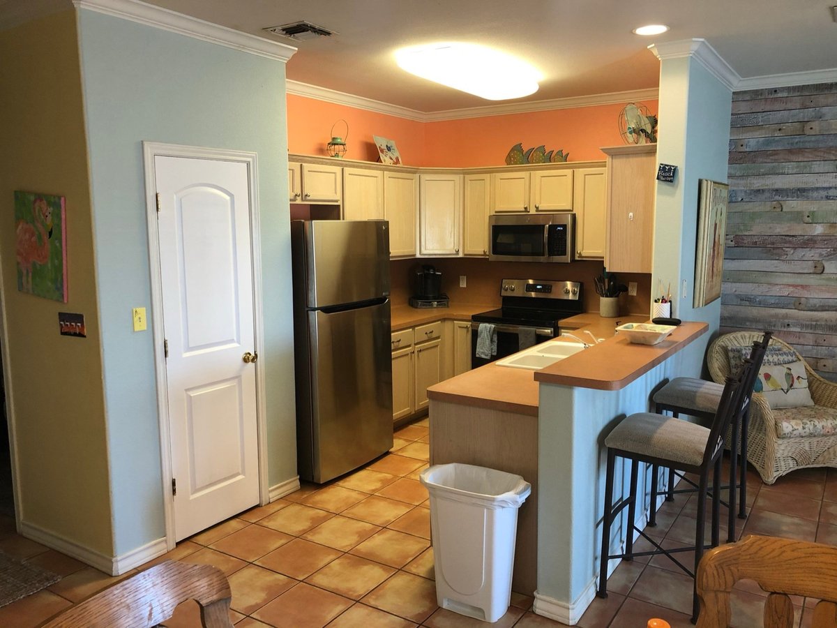 Original kitchen with cream cabinets, orange accent wall, and tile peninsula counter