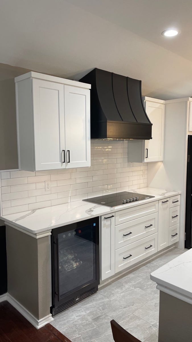 White cabinets and black curved hood over cooktop with built-in wine fridge