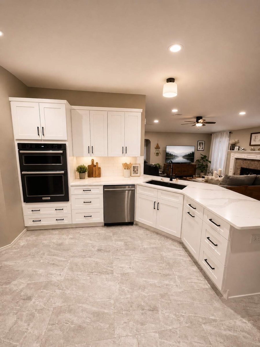 White cabinets, black double ovens, and waterfall peninsula open to living room
