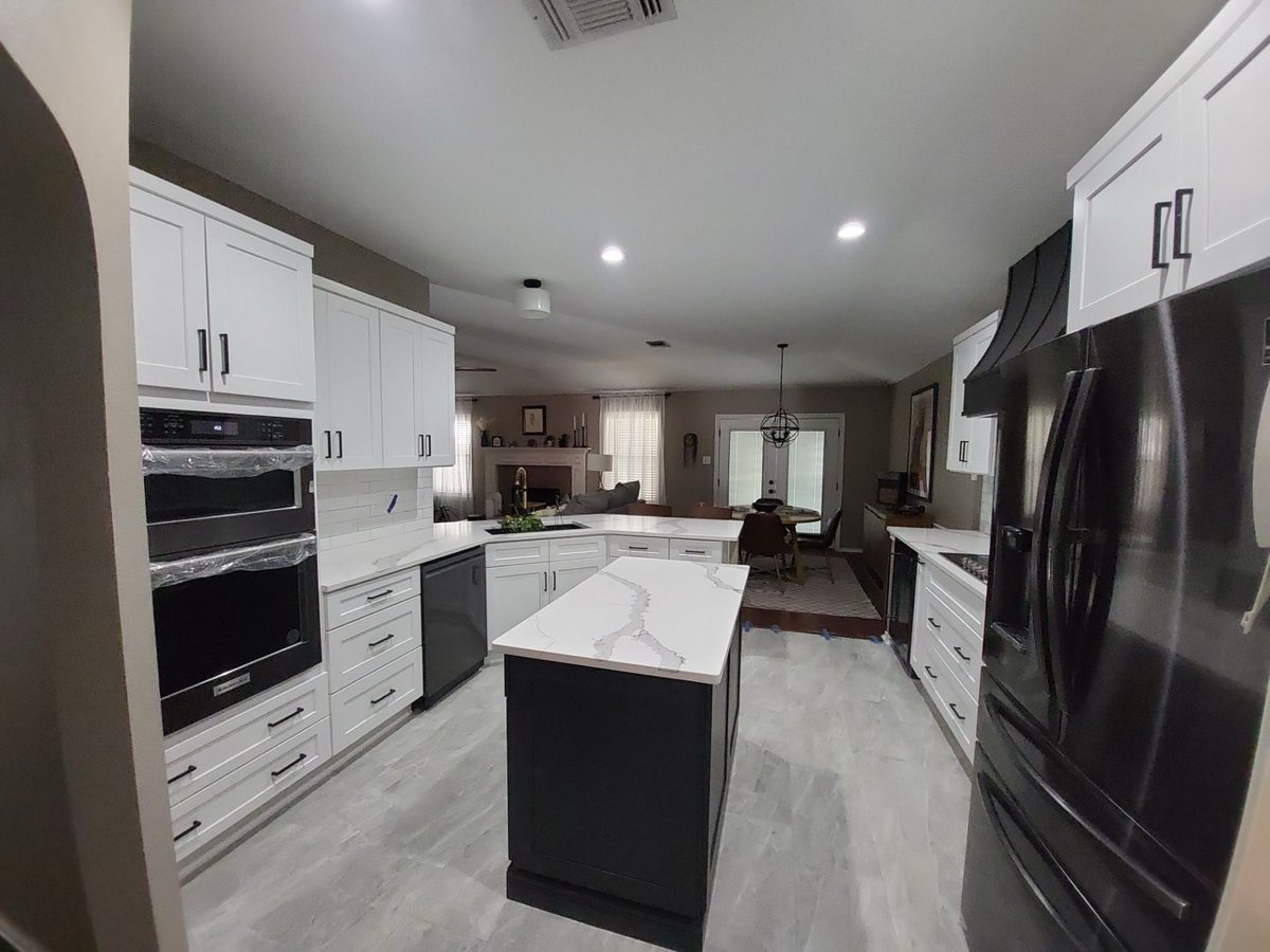 Wide kitchen with white cabinets, black island, double ovens, and gray tile floor