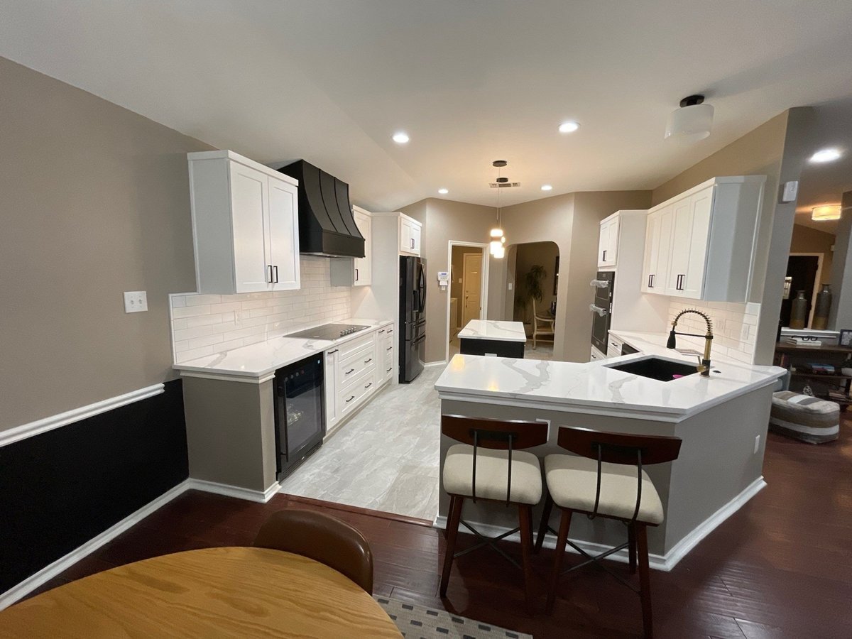 Open kitchen with white cabinets, black hood, and quartz peninsula with stools