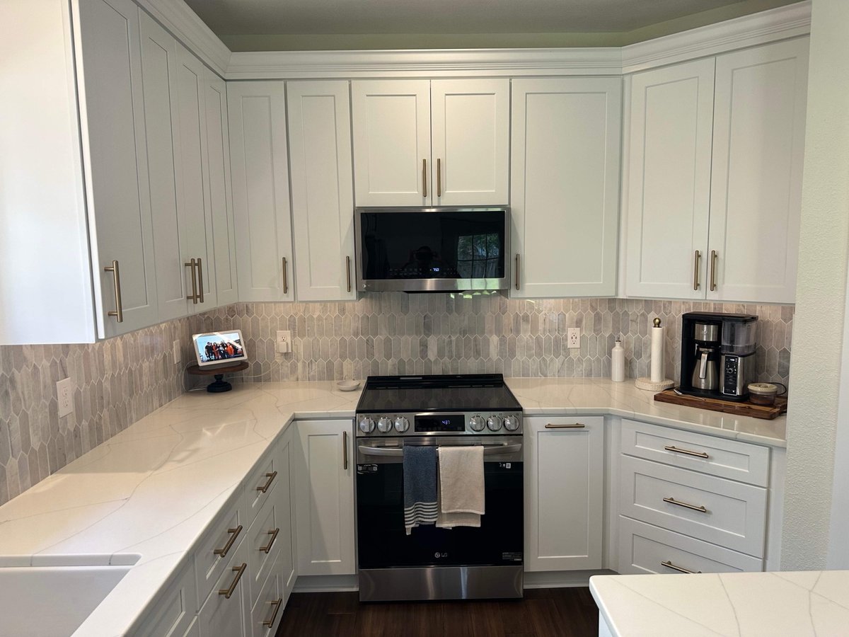 White undermount sink with gold faucet below a window with potted plants