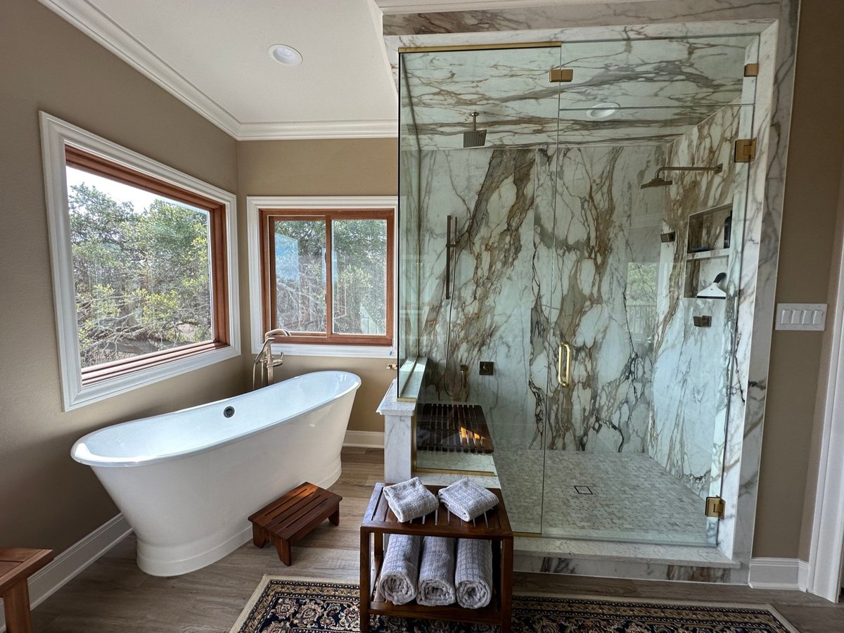 Freestanding soaking tub next to a book-matched marble walk-in shower