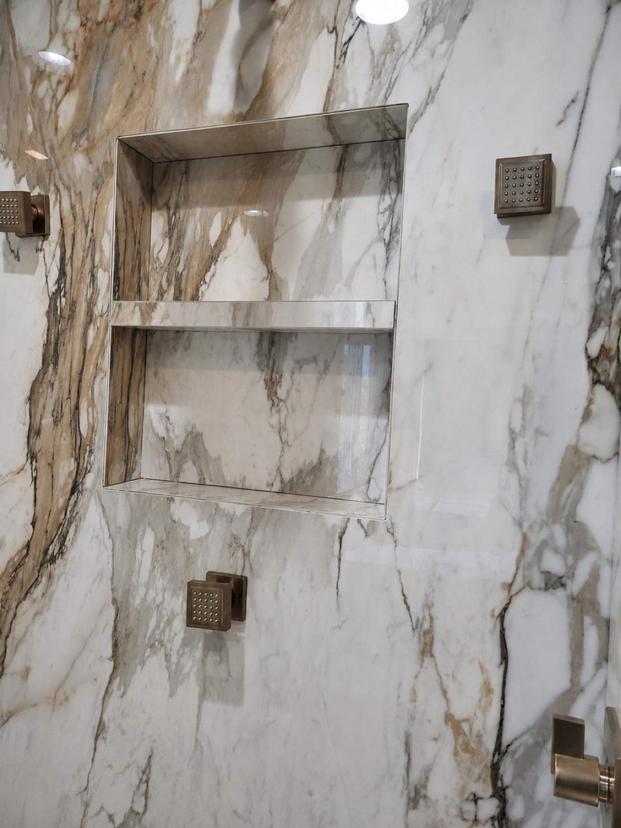 Recessed marble shower niche framed by veined slab and brass body jets