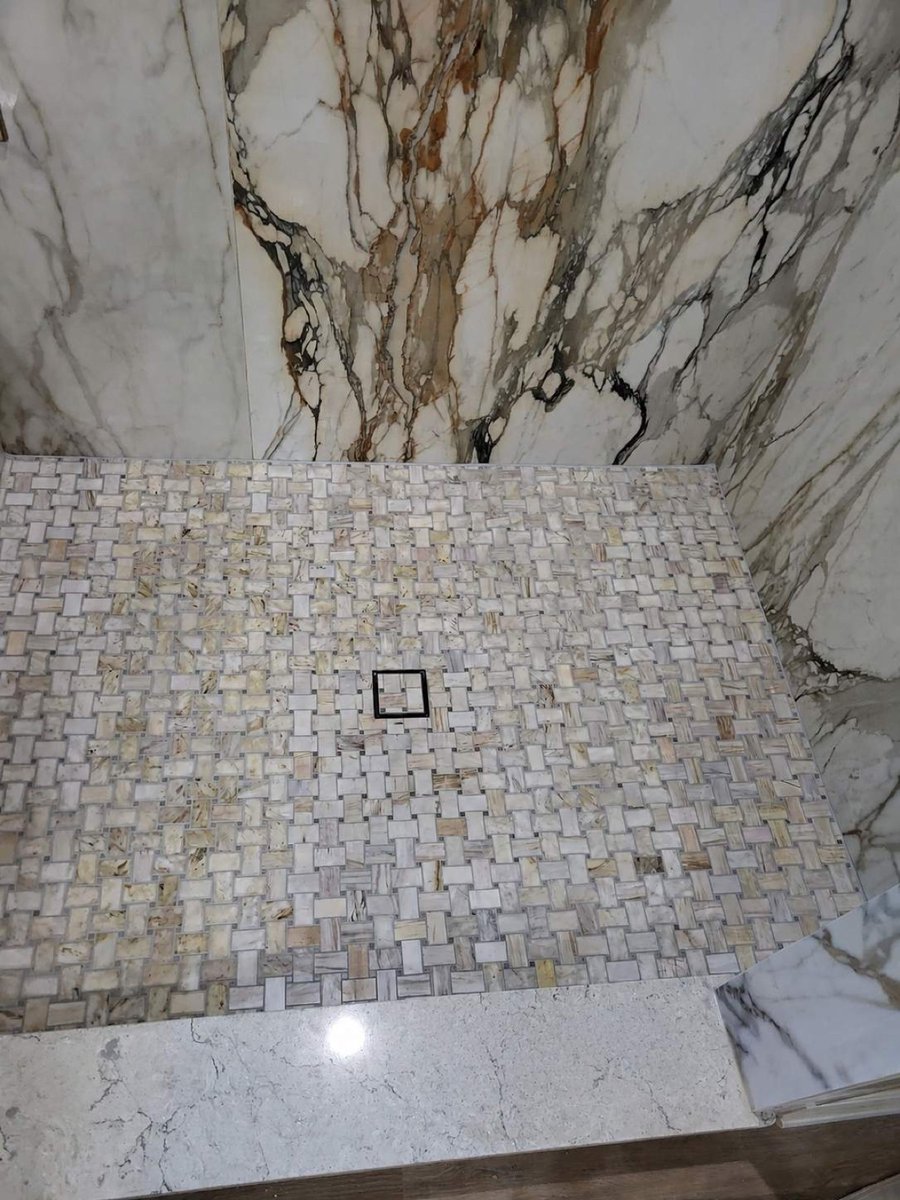 Basketweave mosaic shower floor with center drain against book-matched marble