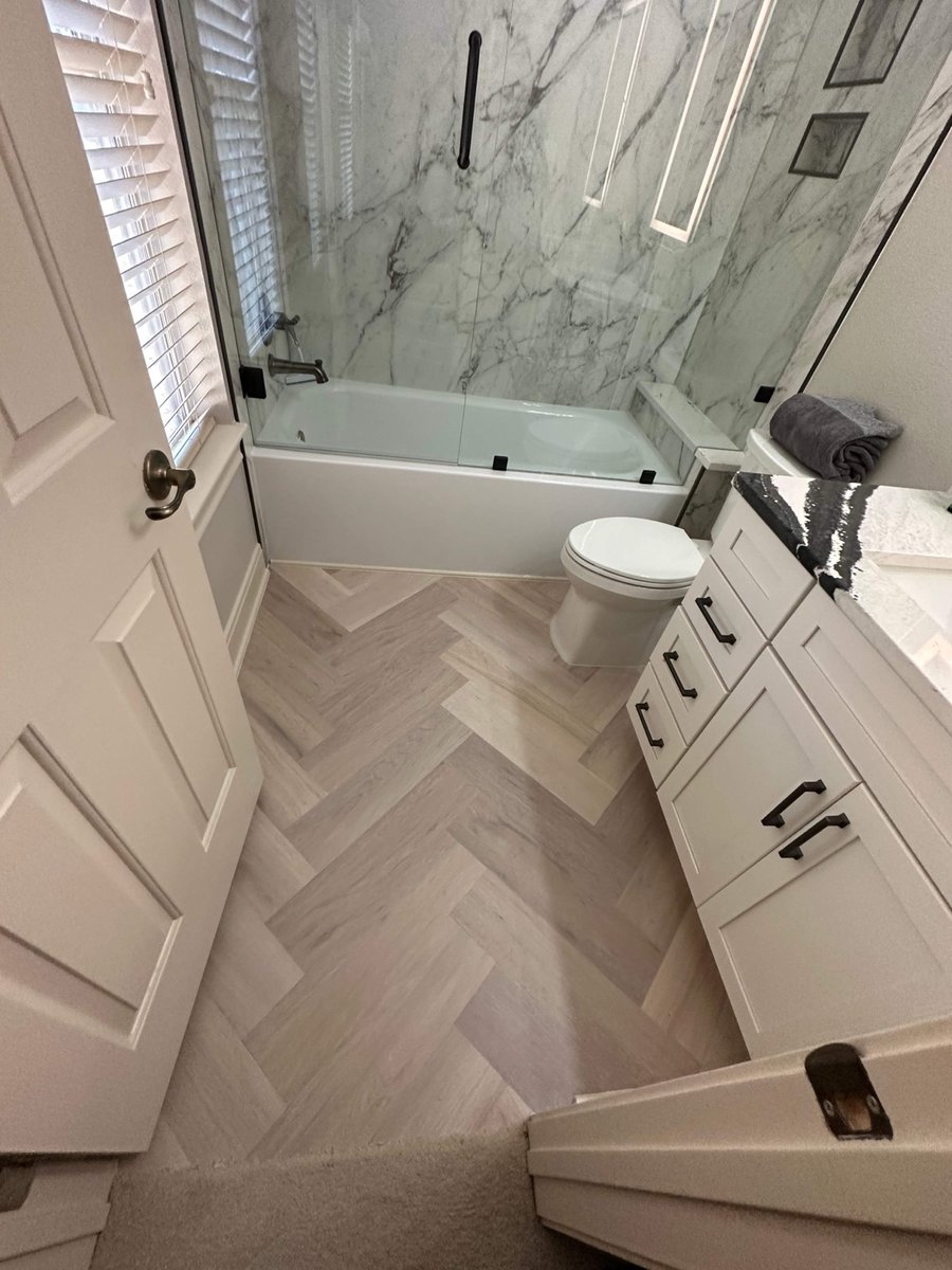 Tub-shower with marble walls and herringbone wood-look floor by a paneled door