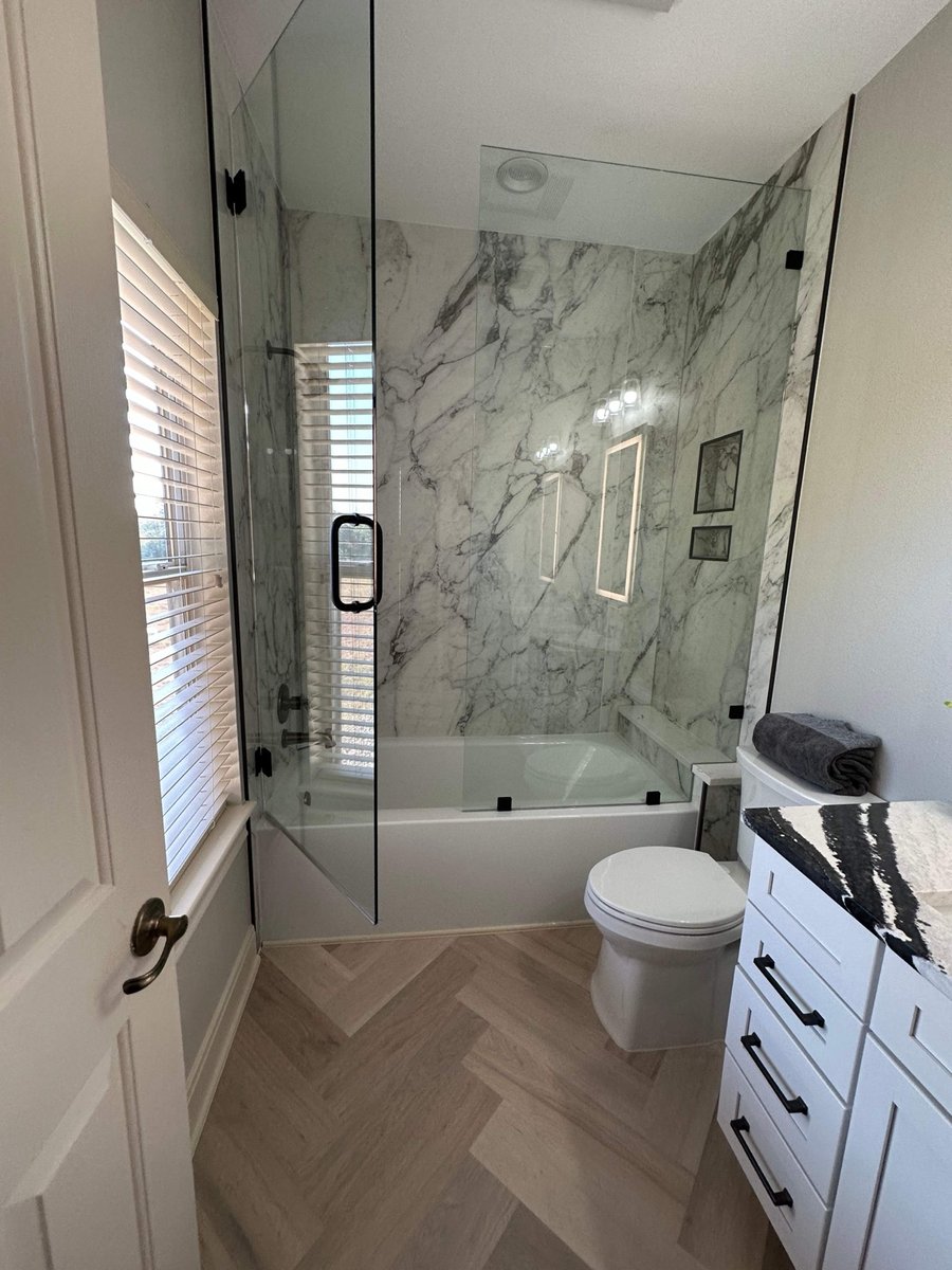 Glass-enclosed marble tub shower with white vanity and herringbone floor