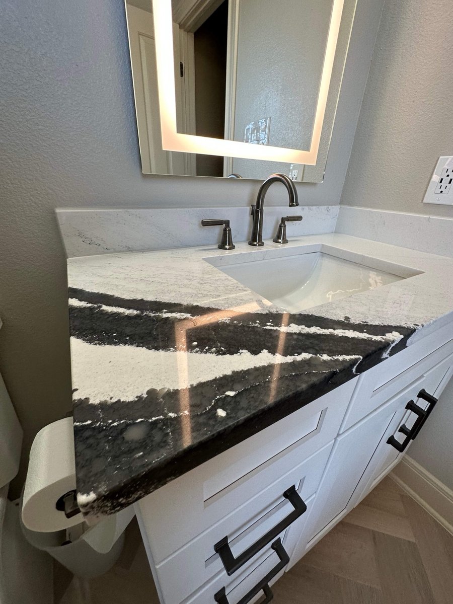 Dramatic black and white veined countertop on a white vanity with lighted mirror