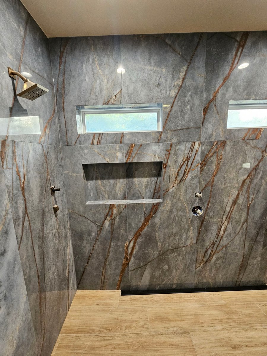Walk-in shower with dramatic gray and copper marble walls and wood-look floor