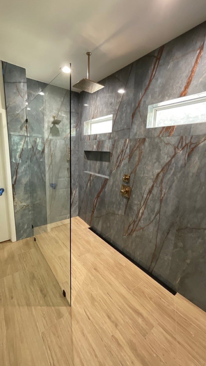 Frameless glass walk-in shower with gold rainfall head and gray marble walls