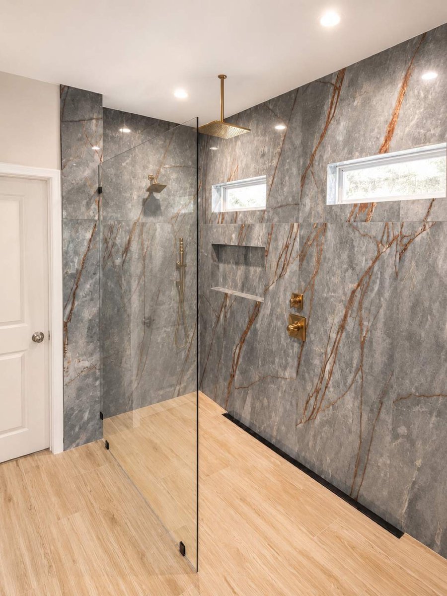Doorless marble shower with gold rainfall fixtures and wood-look tile floor