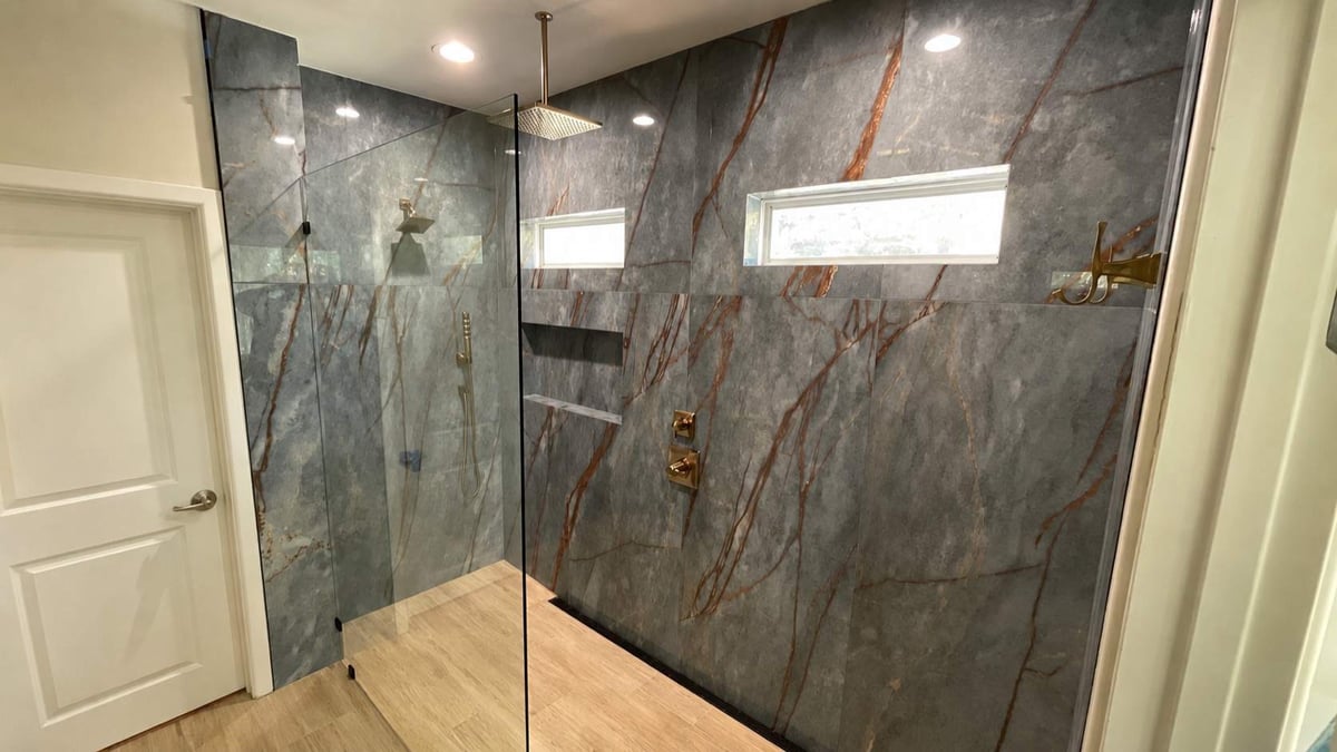 Glass-divided walk-in shower with gray marble walls and gold rainfall head