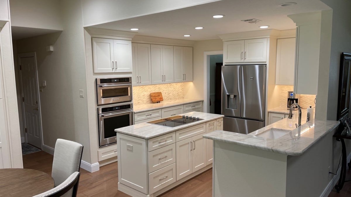 White shaker kitchen with marble island, wall ovens and stainless refrigerator