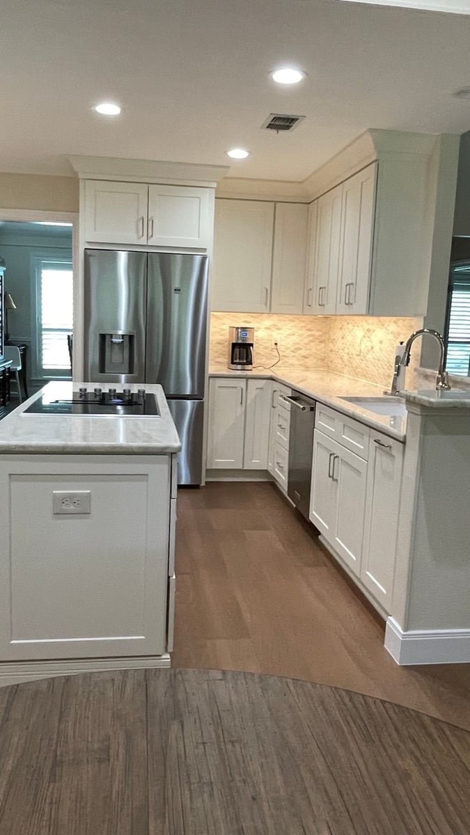 White shaker kitchen island with marble top, wall ovens and stainless fridge