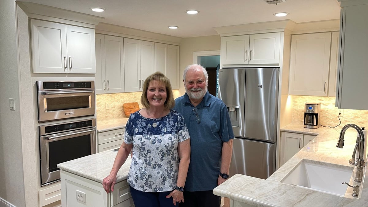 Smiling couple standing in their finished white kitchen with marble counters