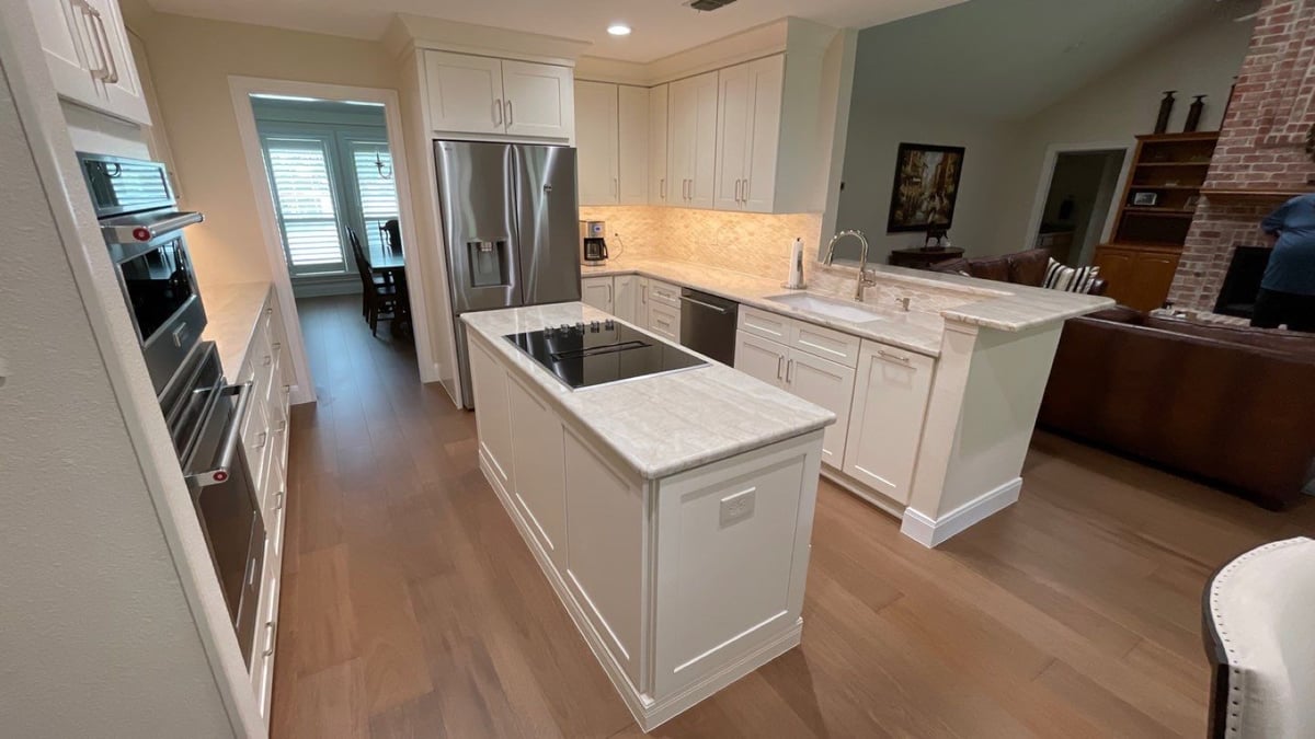 White kitchen with marble island cooktop, peninsula sink and double wall ovens