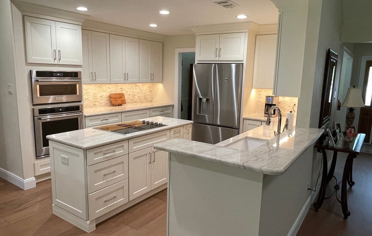 White kitchen with marble peninsula, island cooktop and stacked stainless wall ovens