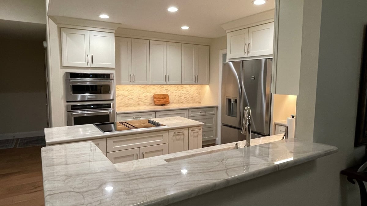 Marble peninsula overlooking white kitchen with wall ovens and stainless fridge