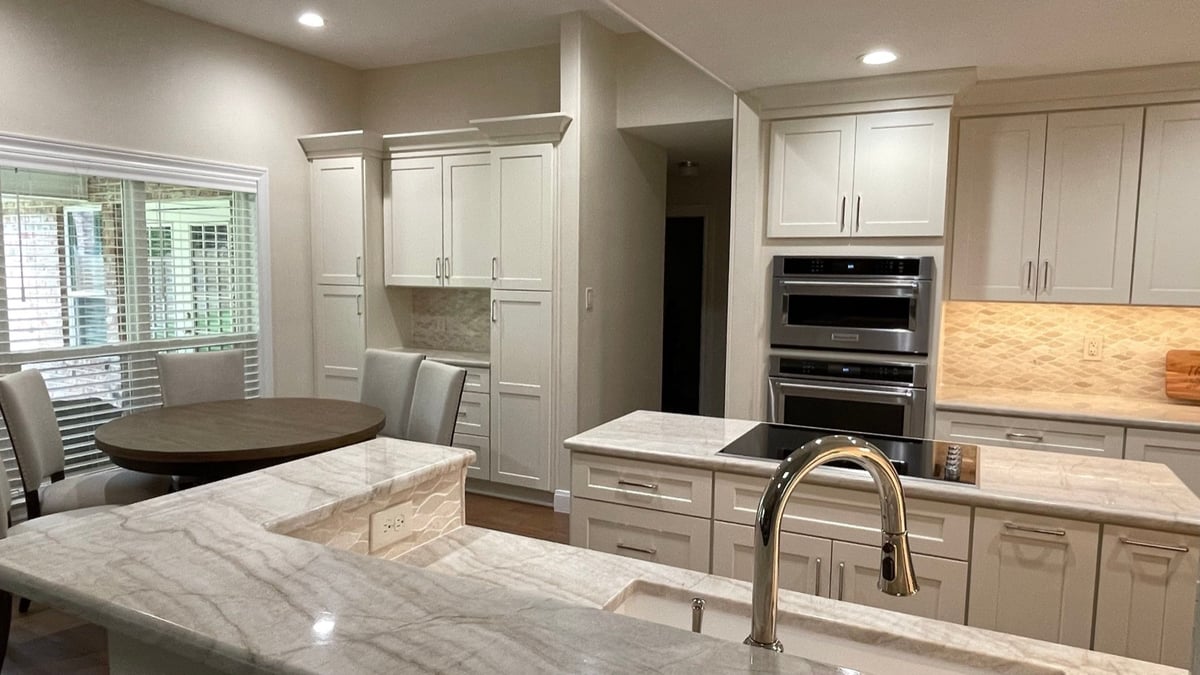 Open white kitchen with marble counters, island cooktop and breakfast table by window