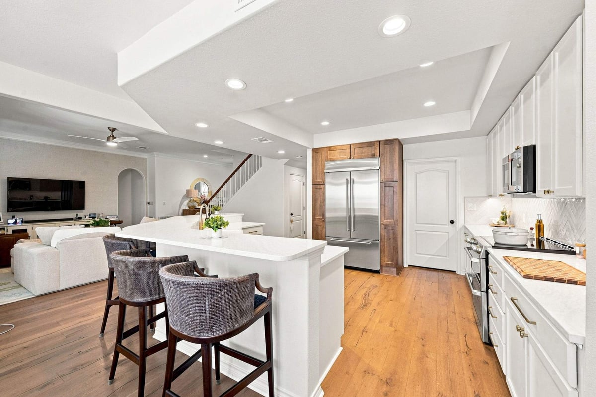Wide view of Deerfield kitchen remodel with white cabinetry, warm wood accents, island, and adjoining beverage bar.