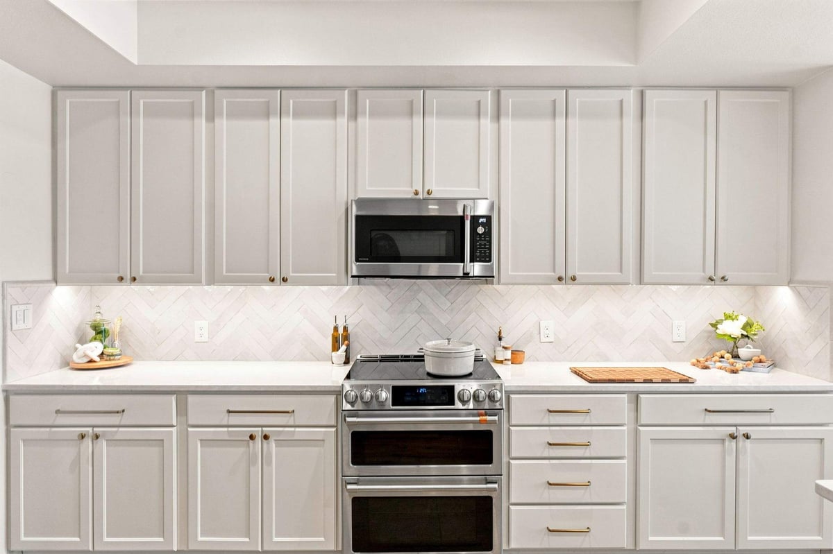 Remodeled kitchen showing white Shaker cabinets, wood cabinetry accents, stainless steel appliances, and herringbone backsplash.