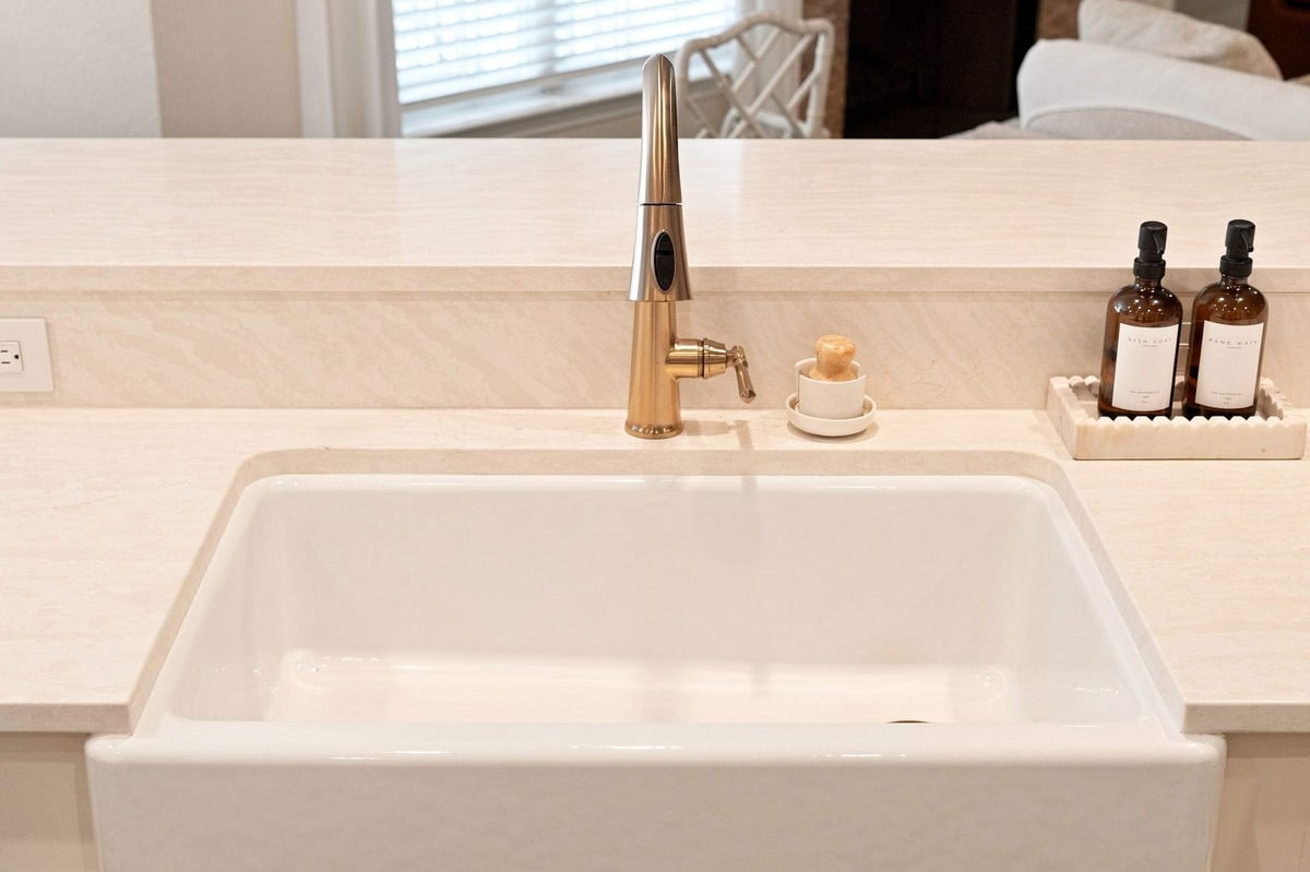 White farmhouse sink with brushed brass faucet and light countertops in a Deerfield kitchen remodel.