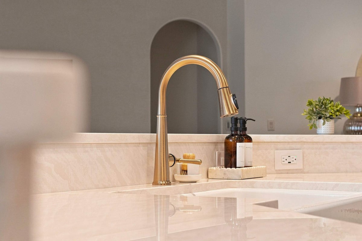 White farmhouse kitchen sink with brass faucet, matching countertop, and soap dispensers.