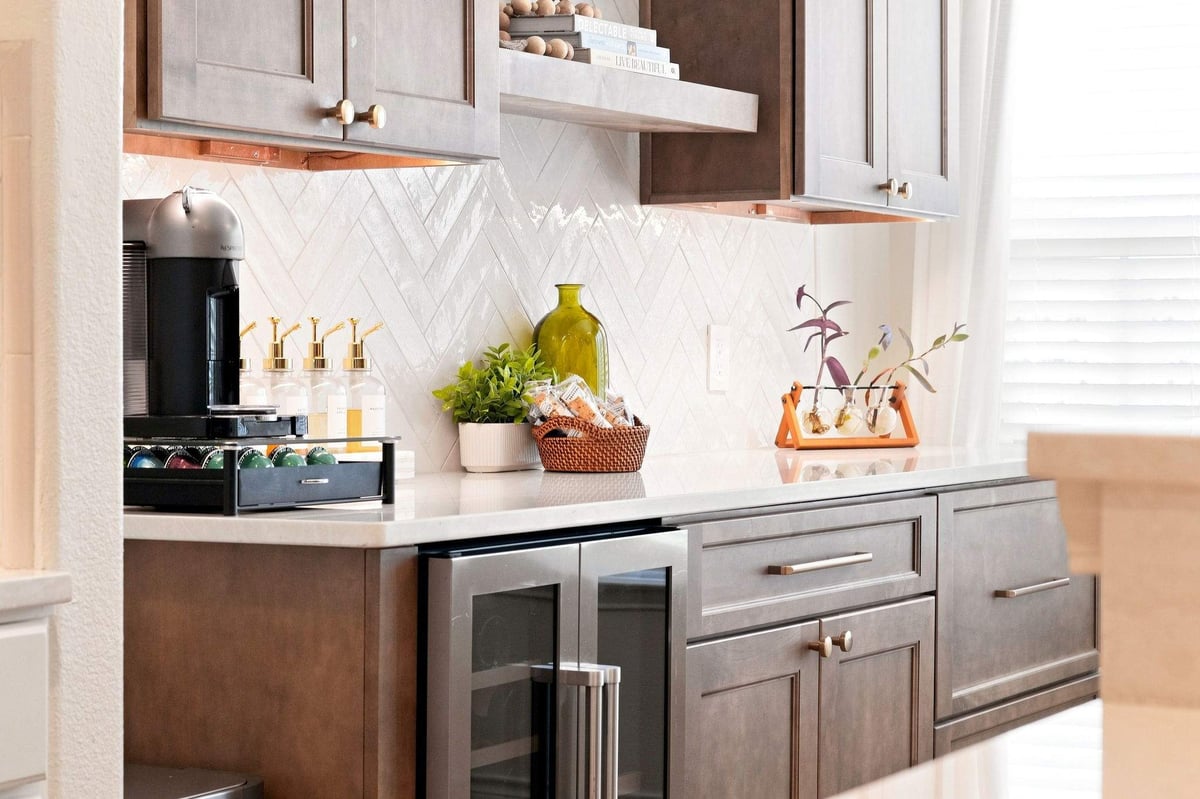 Wood cabinetry and floating shelves above a herringbone backsplash and undercounter beverage refrigerator.