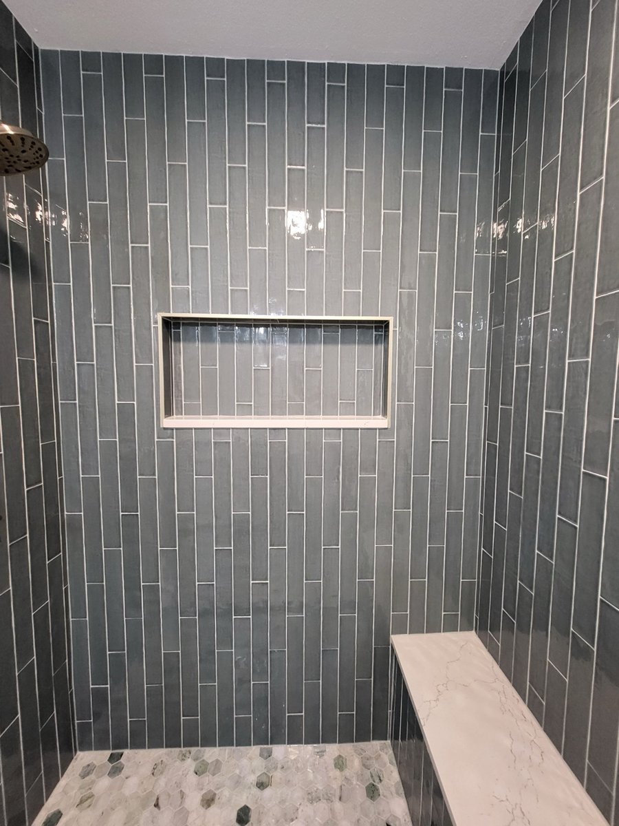 Hexagon marble shower floor and brass drain against blue subway tile
