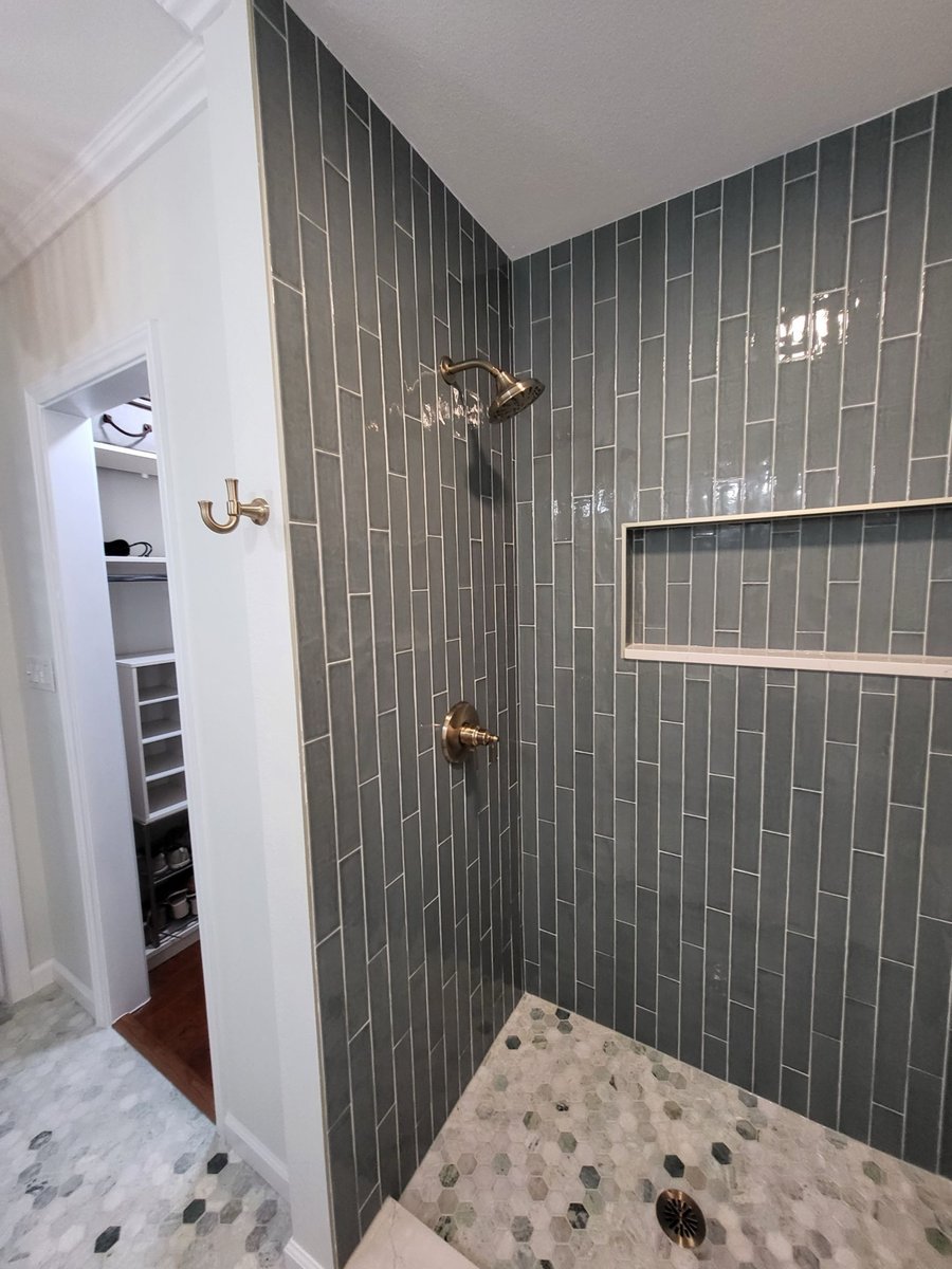 Brushed gold pressure valve trim on blue-gray vertical subway tile